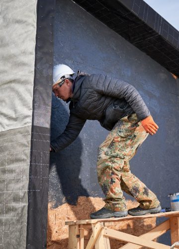 Male painter using paint roller, doing exterior paint work while building wooden frame house.