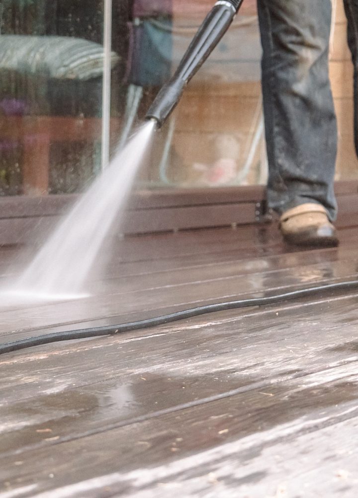 Man cleaning walls and floor with high pressure power washer. Washing terrace wood planks and claddi